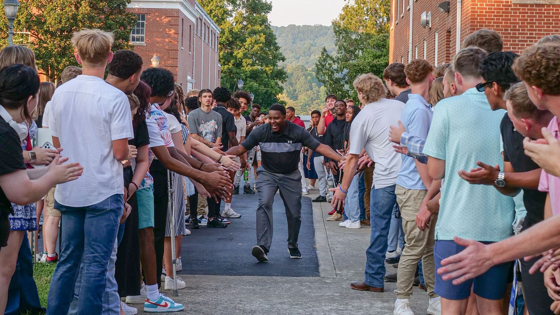 Interim President Dr. DJ Washington is high-fiving through a large crowd of students, faculty, staff, and community members outside the Conway Boatman Chapel before Convocation. A mix of casual and formal attire can be seen from everyone present.