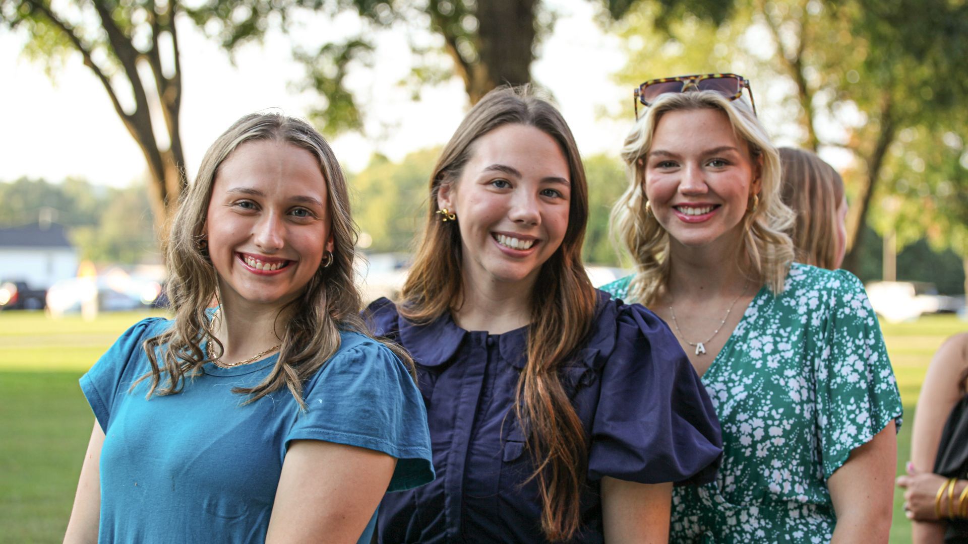 Three female Union Commonwealth University students are posing for a photo in the evening outside the Conway Boatman Chapel. They are standing one behind the other, all smiling and dressed in formal attire.