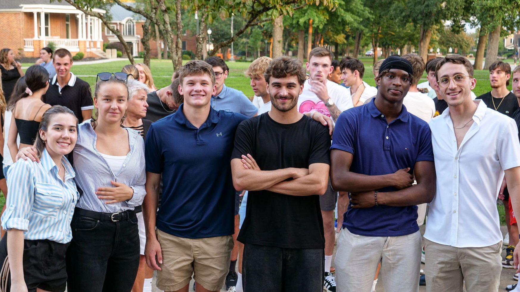A group of six Union Commonwealth University students dressed in business-casual attire for Convocation stand shoulder-to-shoulder outside the Conway Boatman Chapel, smiling among a larger gathering of students, faculty, staff, and community members.