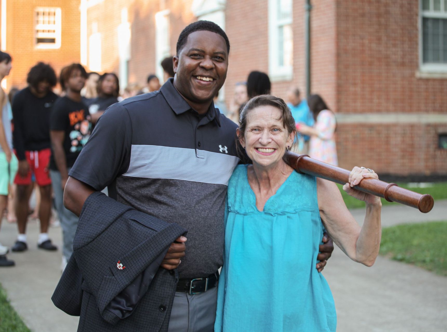 Interim President Dr. DJ Washington and Dr. Christine Marley-Frederick pose outside the Conway Boatman Chapel before Convocation. Marley-Frederick holds the wooden ceremonial mace over her shoulder. A crowd is visible in the background.