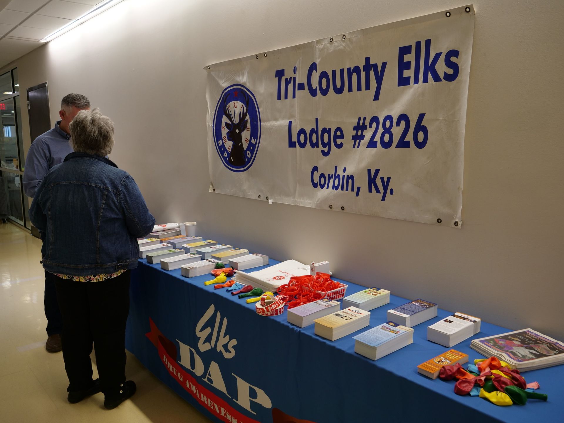 Informational display from Tri-County Elks wherein wrist bands, pamphlets, booklets, and uninflated balloons are placed together on a blue table.