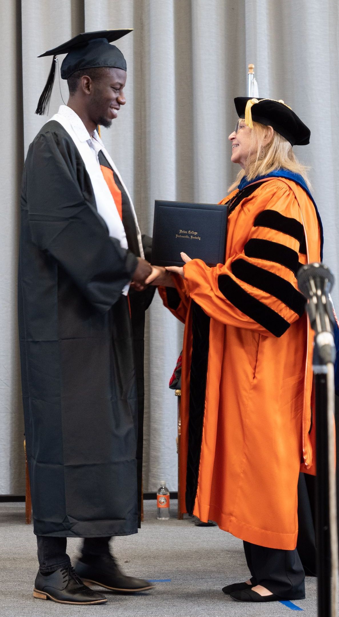 President Marcia Hawkins handing Nijah Smith his diploma while shaking his hand on stage.