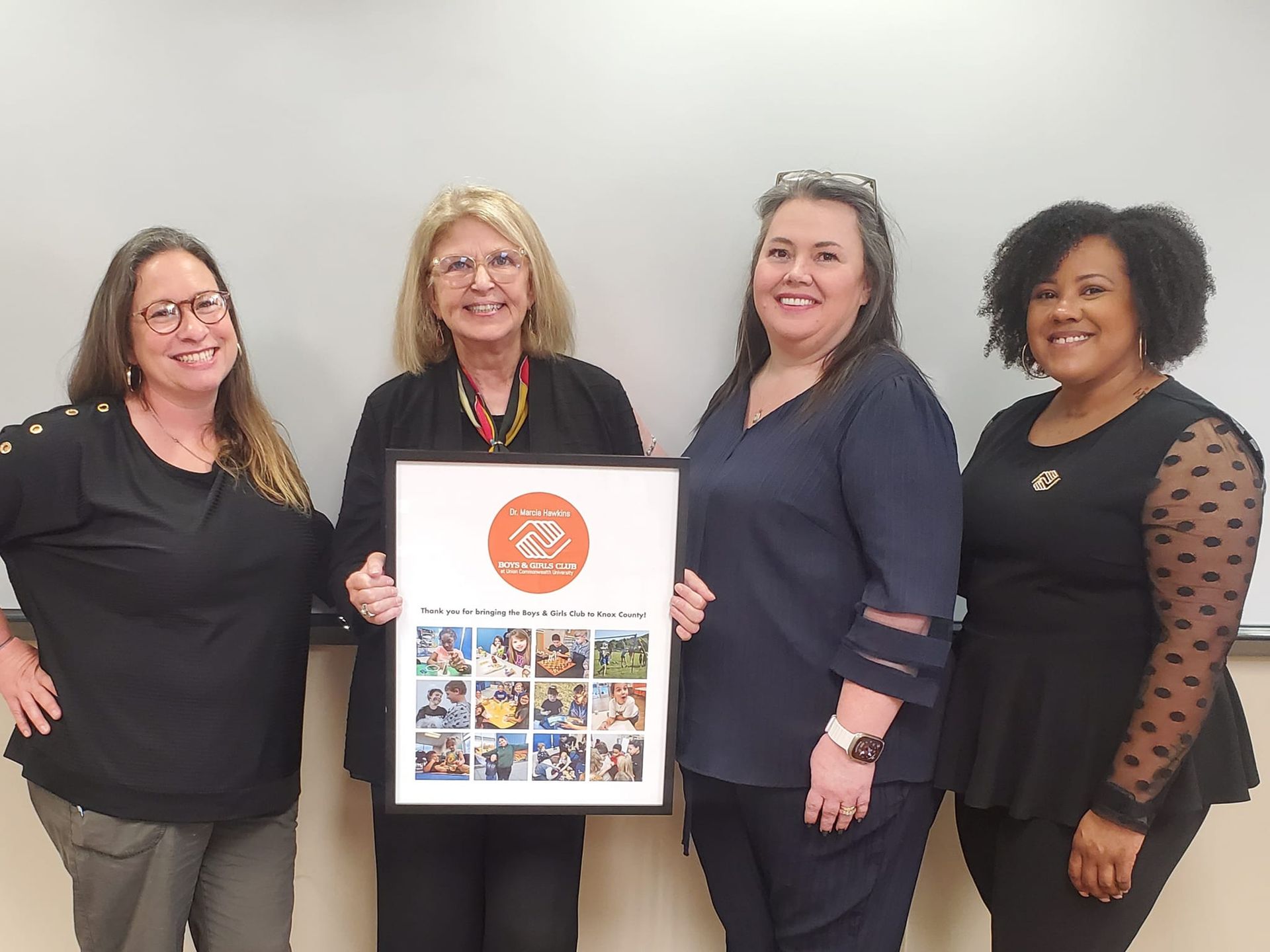 From left to right, Erica Pearson, Marcia Hawkins, Kateena Haynes, and Kendra Calhoun stand with Hawkins, who is holding a framed poster featuring the new Club logo, pictures of children participating in various club activities, and the words Thank you for bringing the Boys & Girls Club to Knox County!