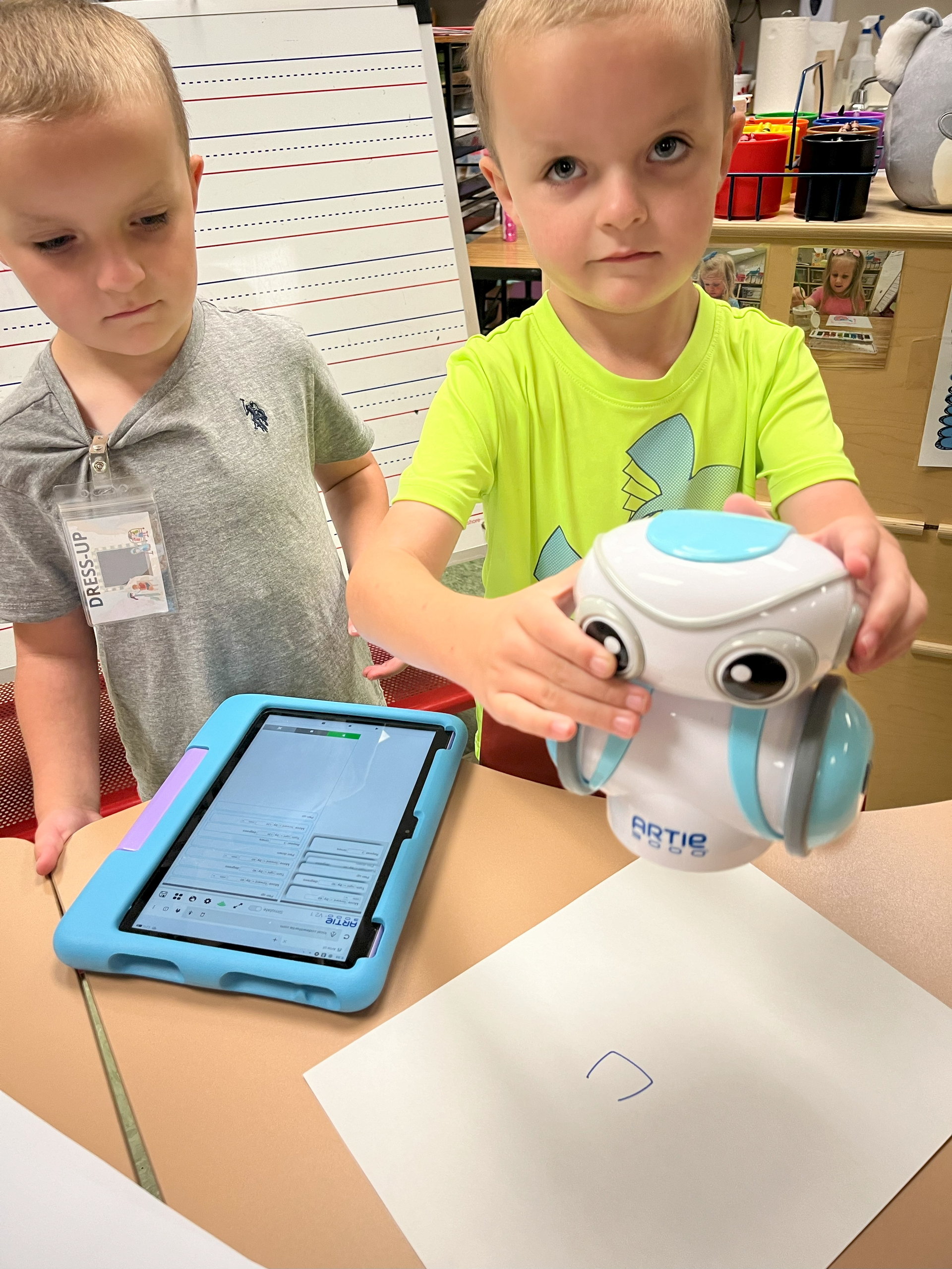 One young boy holds a small robot while the other looks at a kindle fire tablet