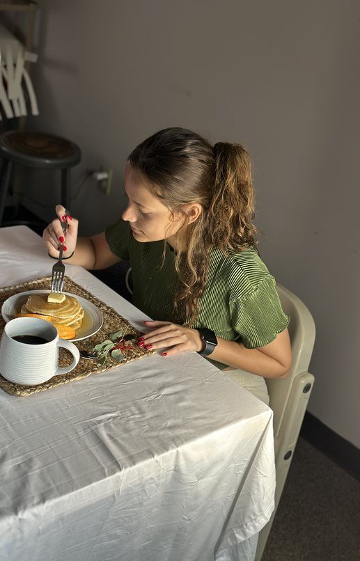 A student sitting in front of a coffee cup and plate filled with pancakes and oranges.