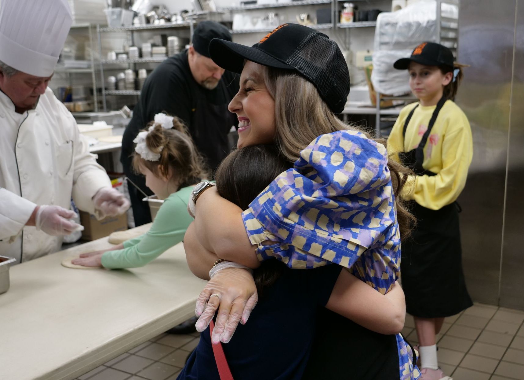 Libby Kate Vaughn hugs a child attendee while other children are flattening dough with Union Dining staff behind them.