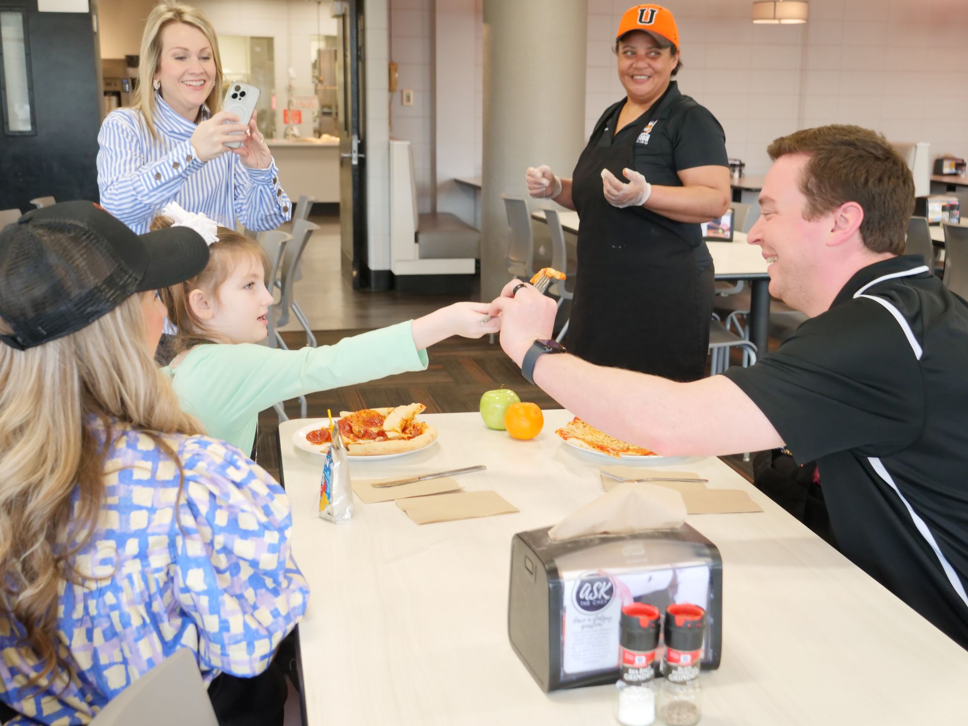 James Becknell shares a slice of pizza with a child attendee while Libby Kate Vaughn, a member of the Union Dining staff, and a parent gather around.