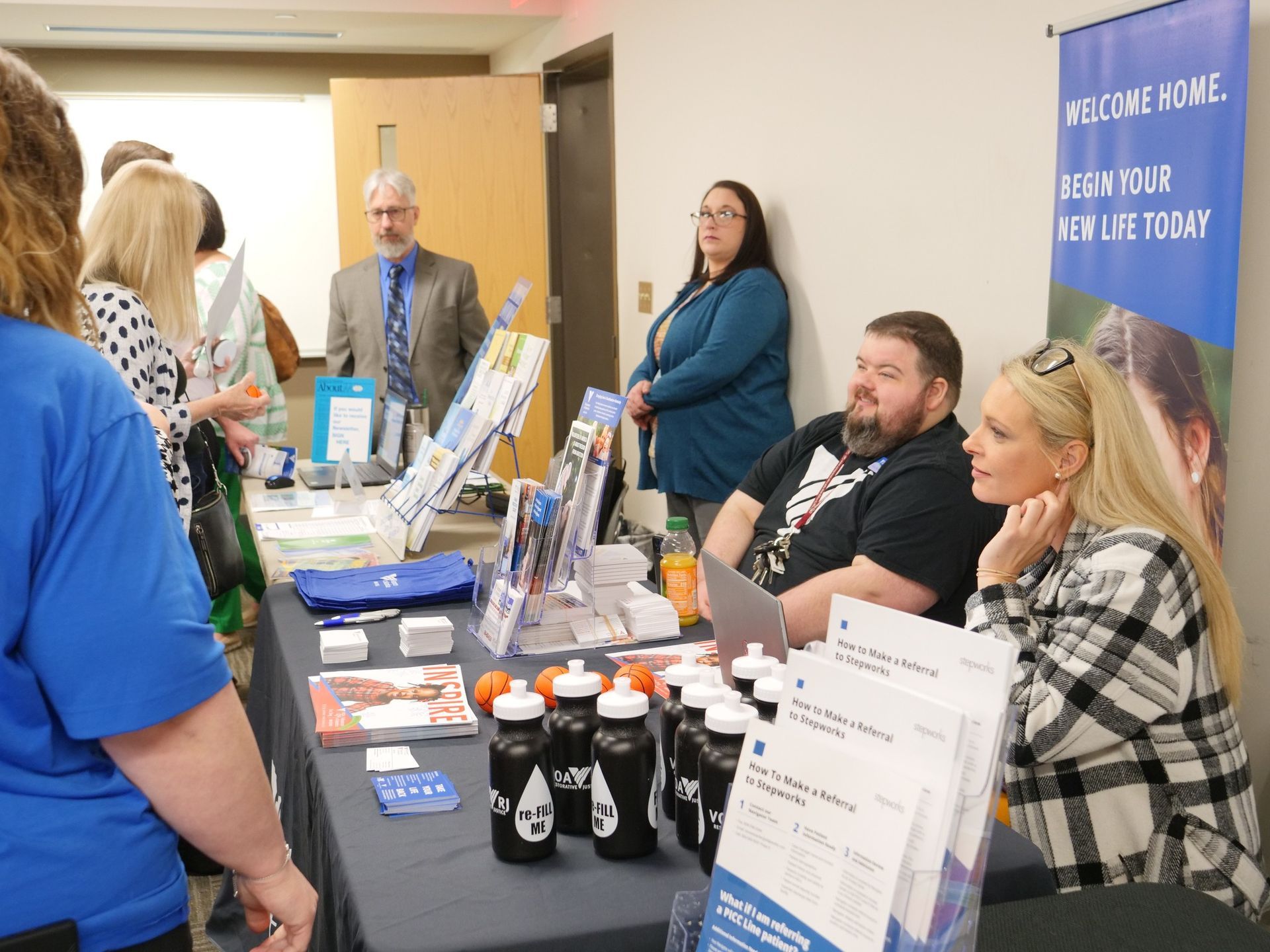 Stepworks providing information and resources at a table filled with items including pamphlets, booklets, bottles, and tiny toy basketballs.