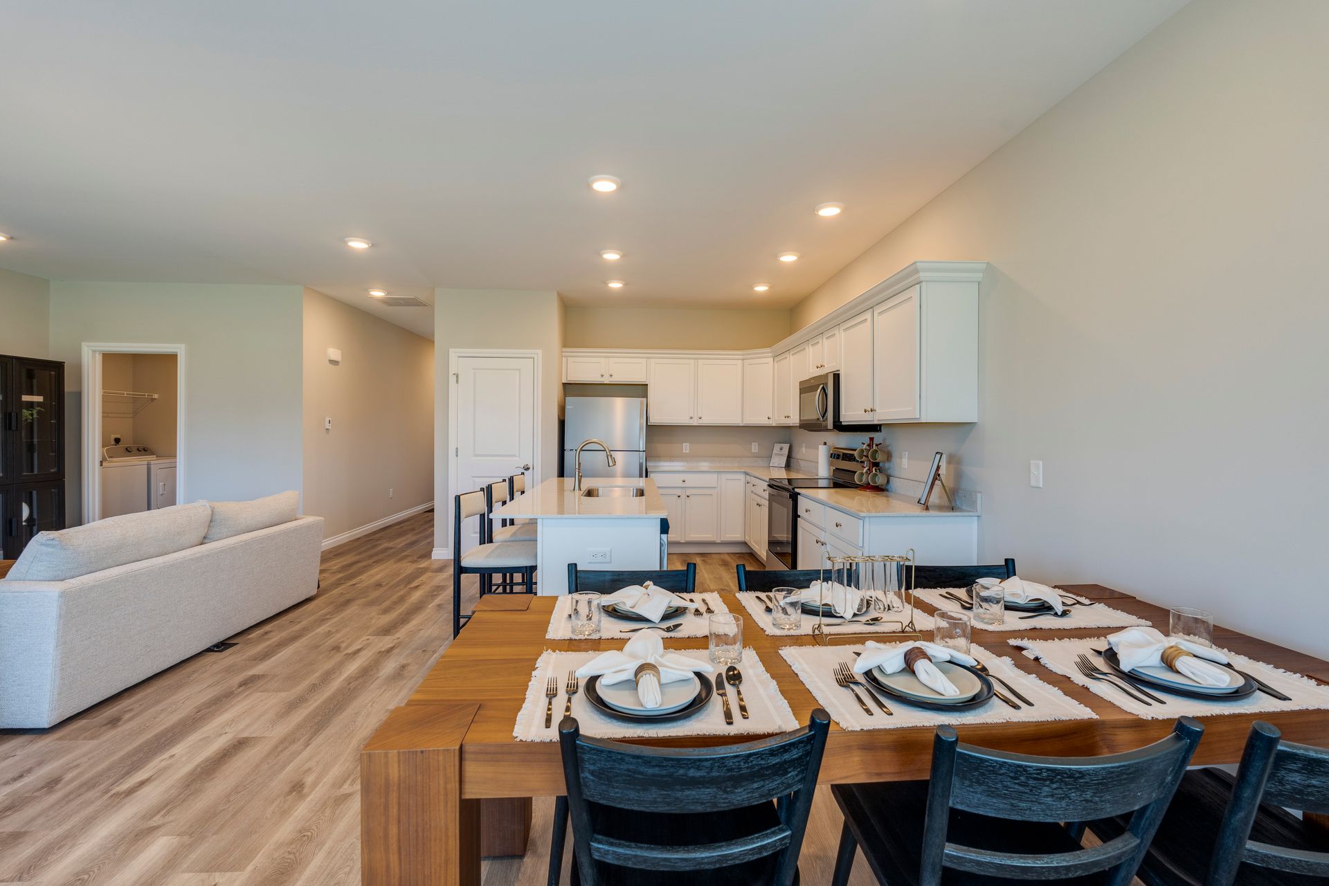 Dining room with a wooden table set for six, open to a kitchen and living area.