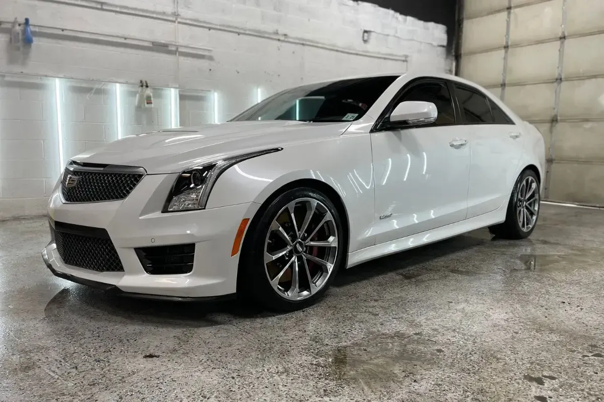 White Cadillac ATS-V sedan in a garage, with chrome wheels and black trim.