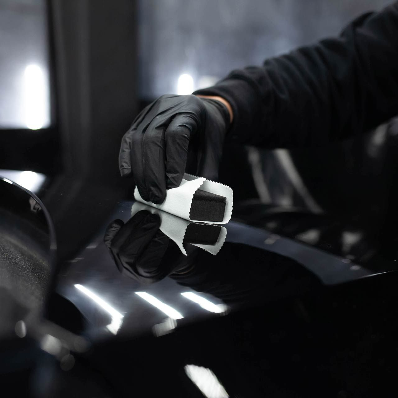 Person in black gloves applying a ceramic coating to a black car.