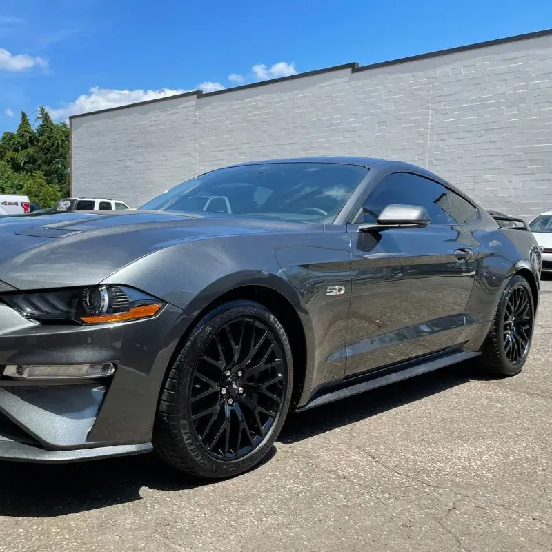 Gray Ford Mustang parked on asphalt with black wheels and a gray building in the background.