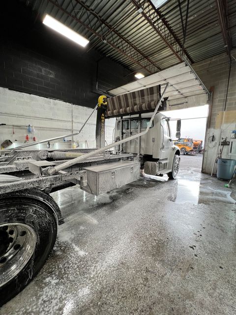 Truck being washed in a bay, covered in soap. Side view, with wheels and frame visible.