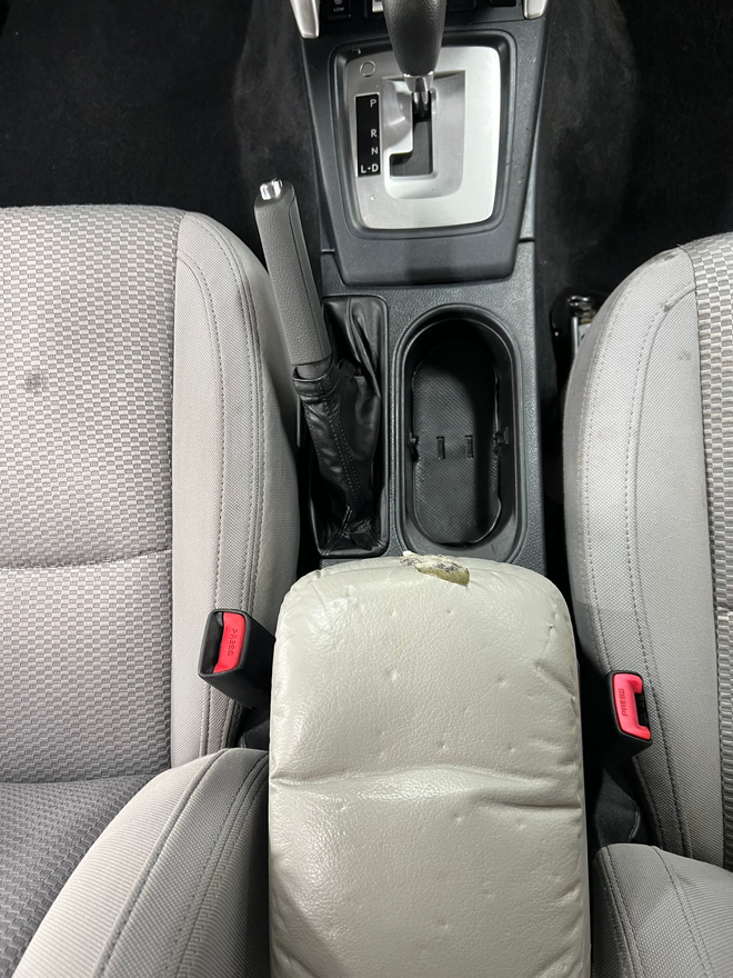 Car interior: gray seats, center console with gear shift, handbrake, cup holder, and armrest.