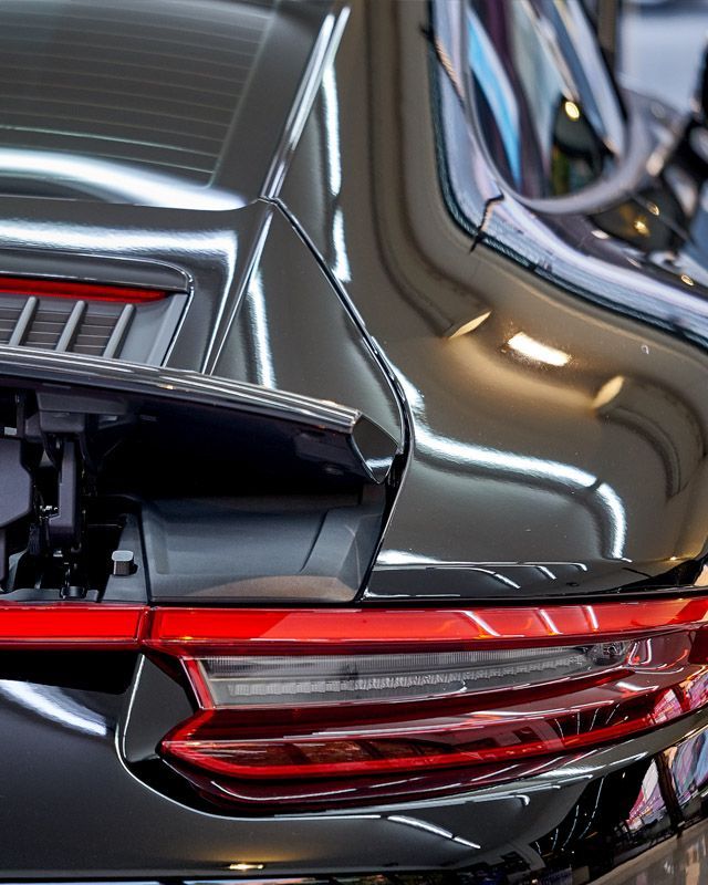 Black Porsche rear end with red taillights, reflecting bright overhead lights.