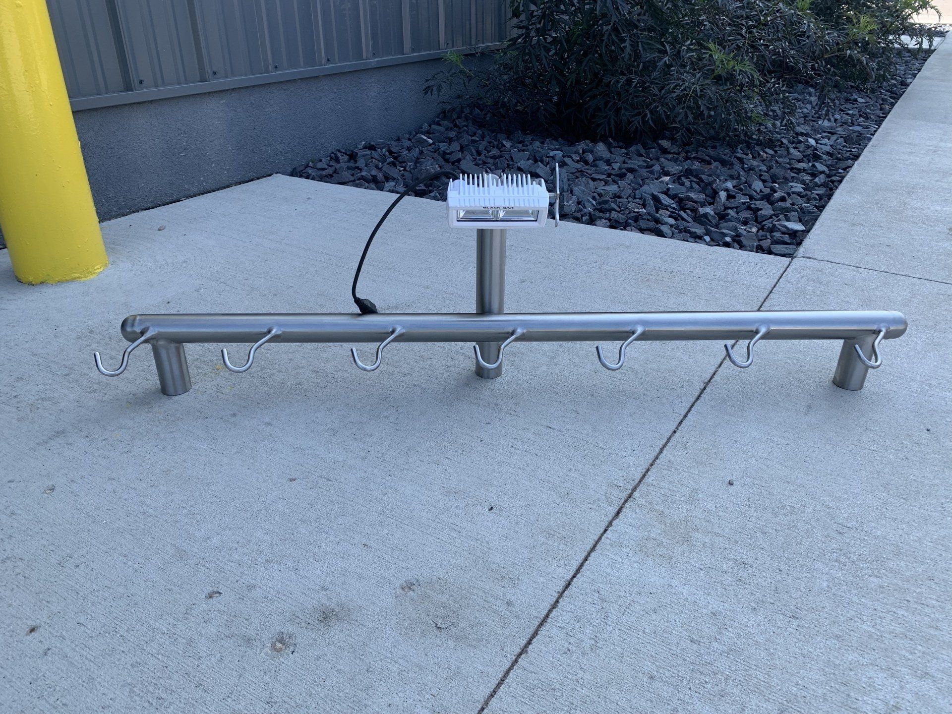 A stainless steel railing with hooks is sitting on a sidewalk.