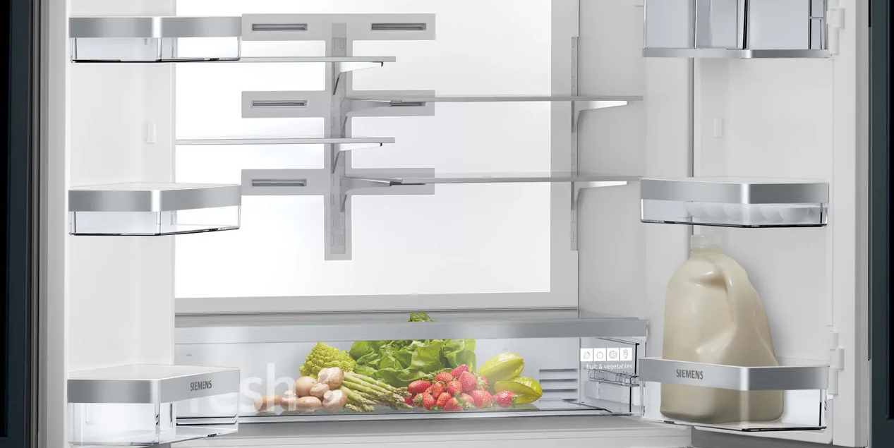 Open refrigerator interior with shelves and fresh produce in the bottom drawer.