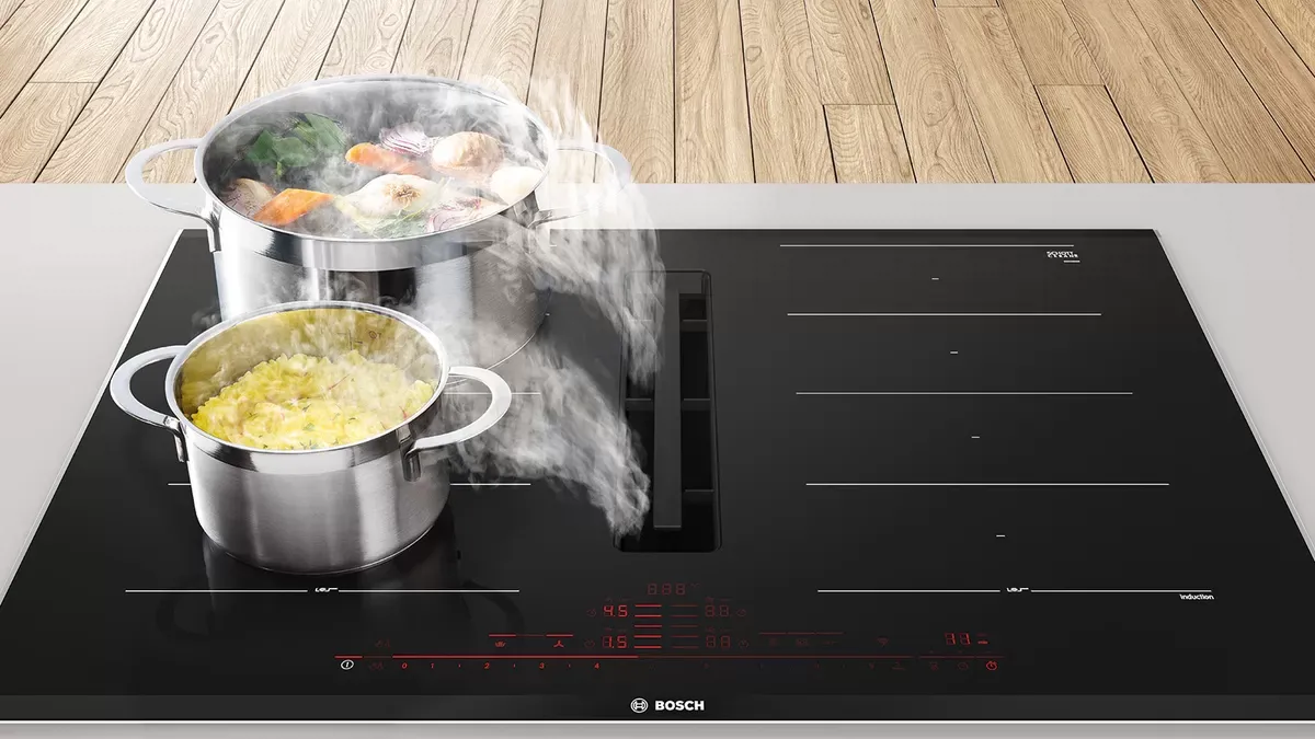 Stainless steel pots on black stovetop, steam rising from food, built-in ventilation.