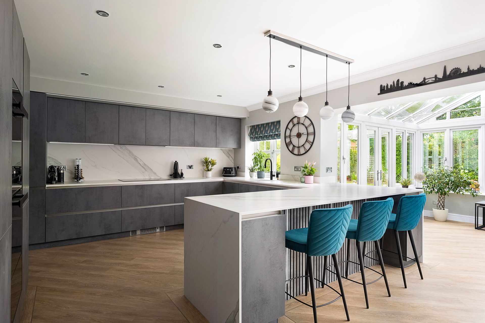 Modern kitchen with grey cabinets, marble countertops, and teal bar stools.
