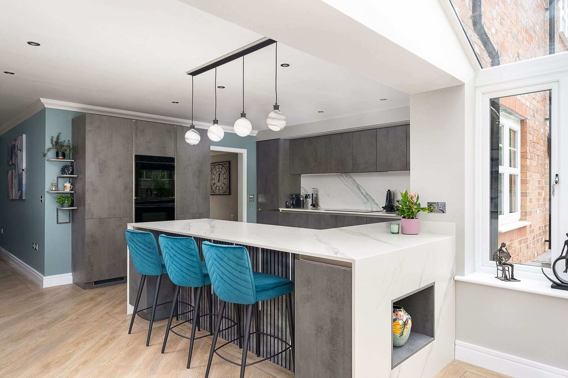 Modern kitchen with a gray island, teal bar stools, and pendant lights.