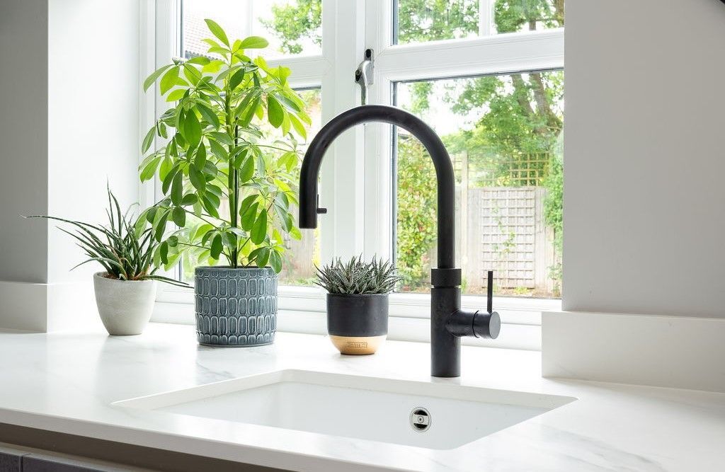 Black kitchen faucet over white sink, next to window with potted plants.