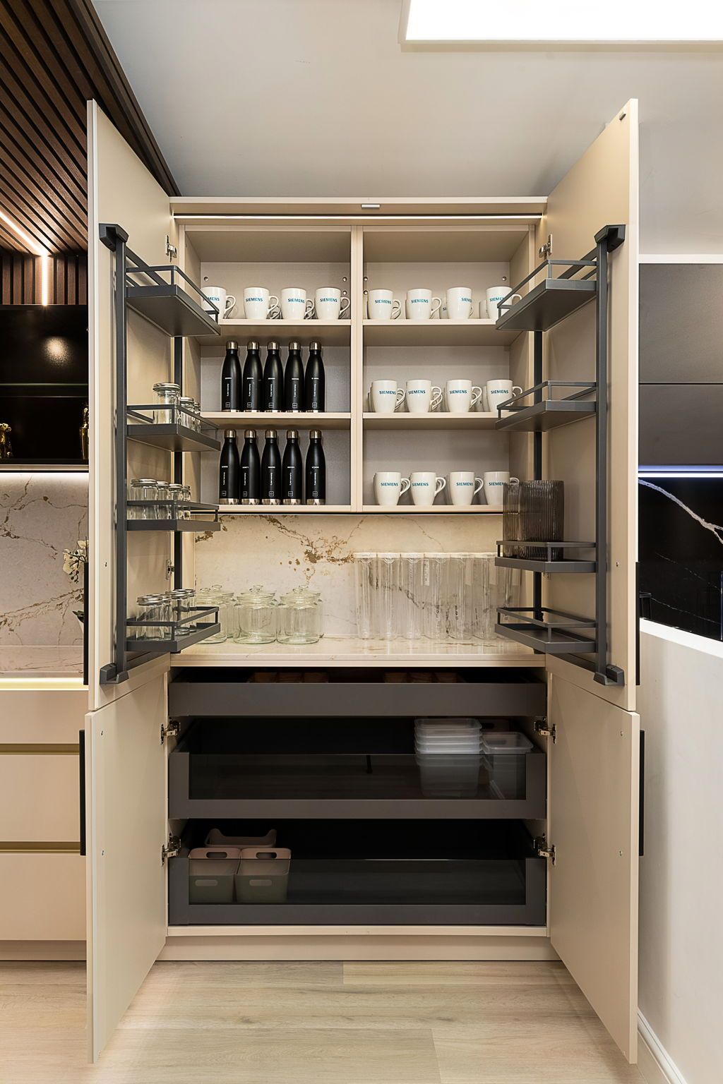 Beige kitchen pantry with pull-out shelving, holding mugs, bottles, and storage containers.