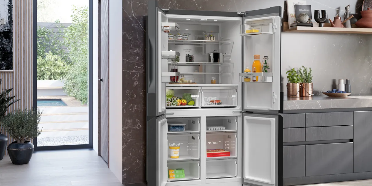 Open refrigerator in modern kitchen, showing shelves of food and beverages. Dark cabinetry and countertops.