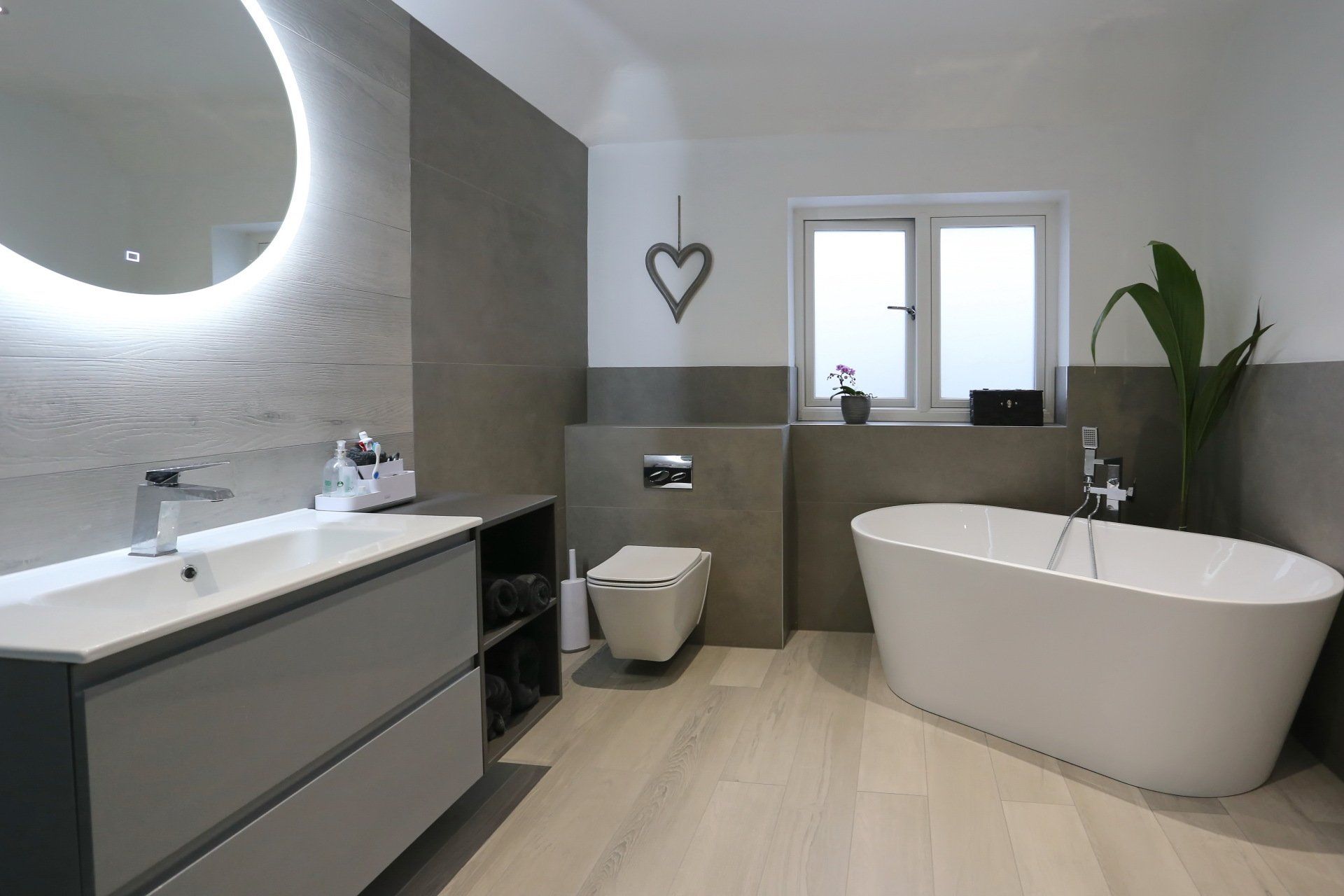 Modern bathroom with gray and white color scheme, floating vanity, freestanding tub, and large round mirror.