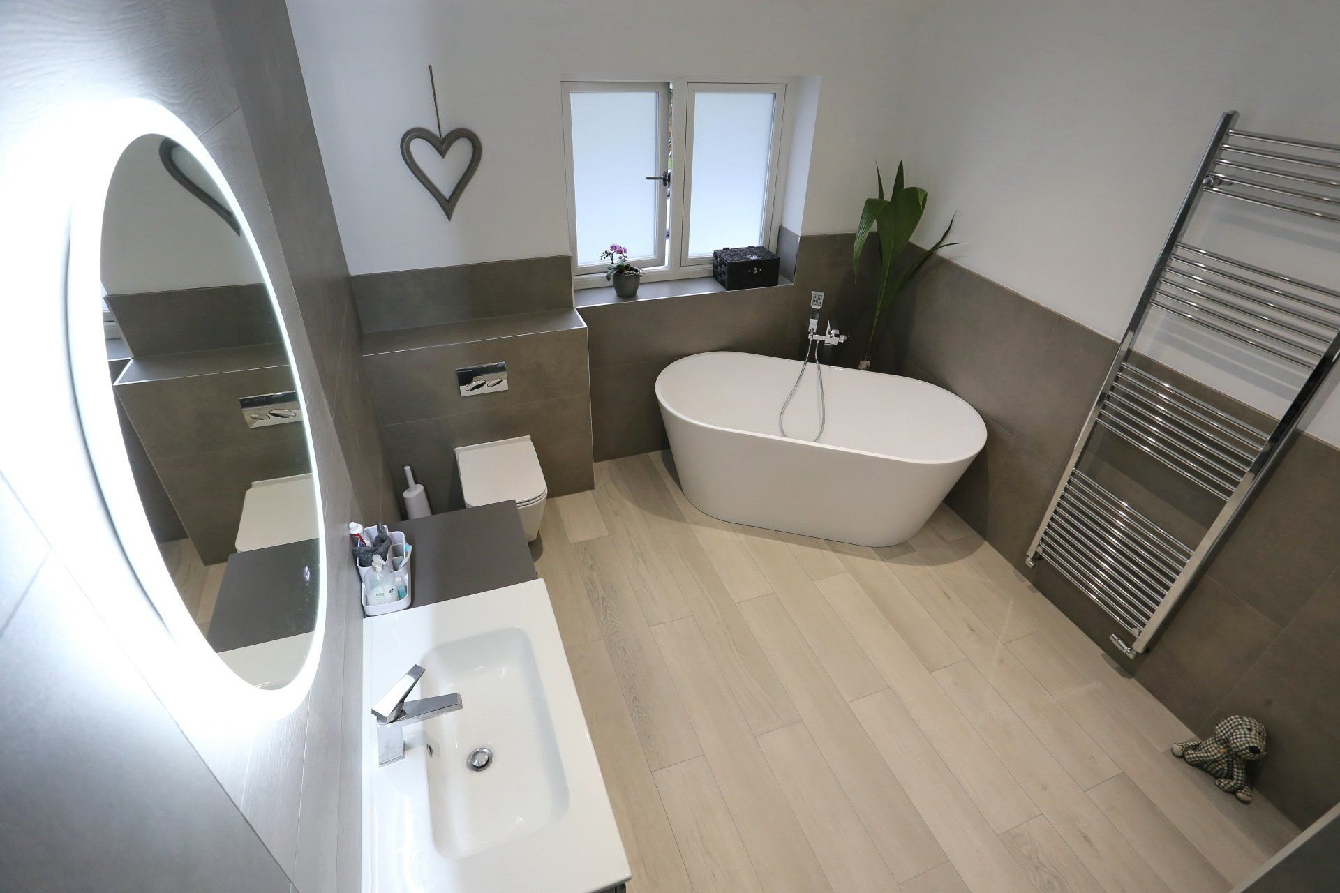 Modern bathroom with freestanding white tub, vanity, and a large circular mirror.