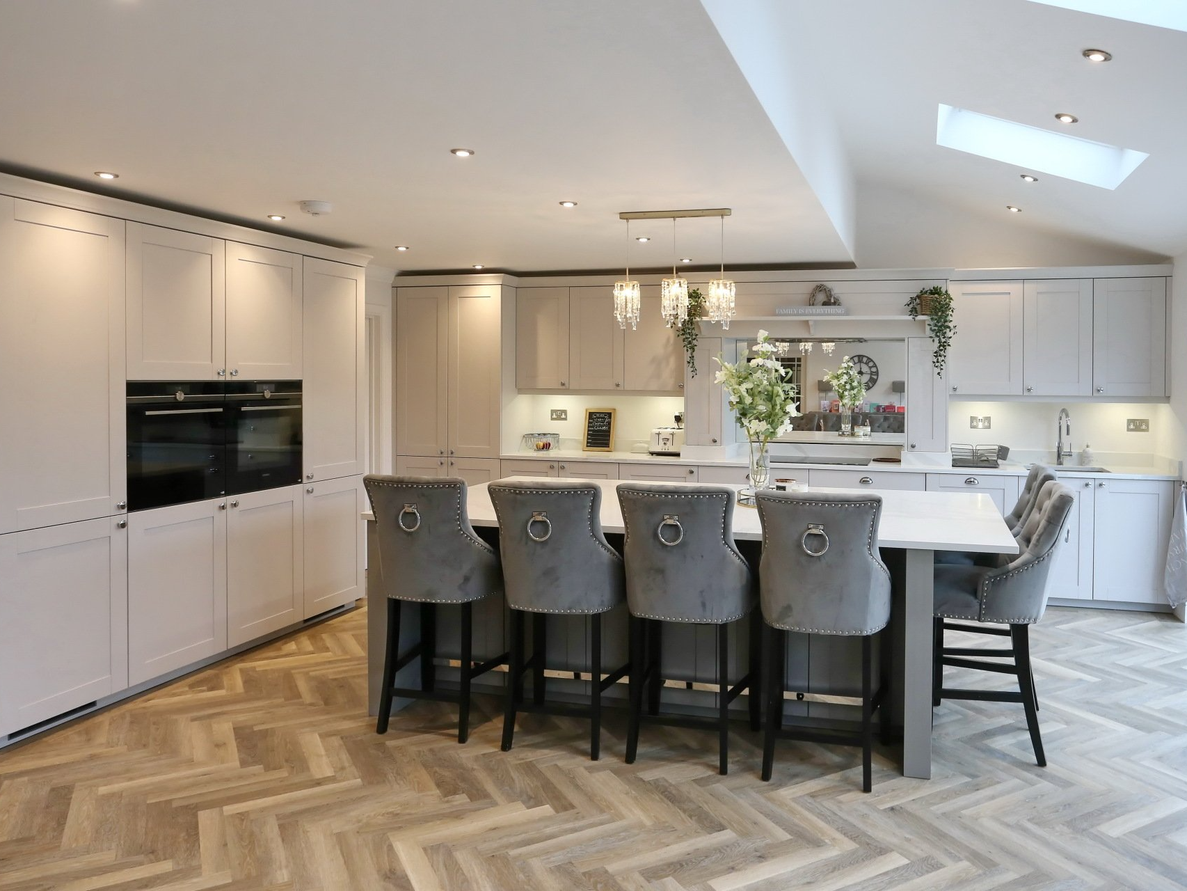 Modern kitchen with light grey cabinetry, island with seating, and herringbone wood floor.