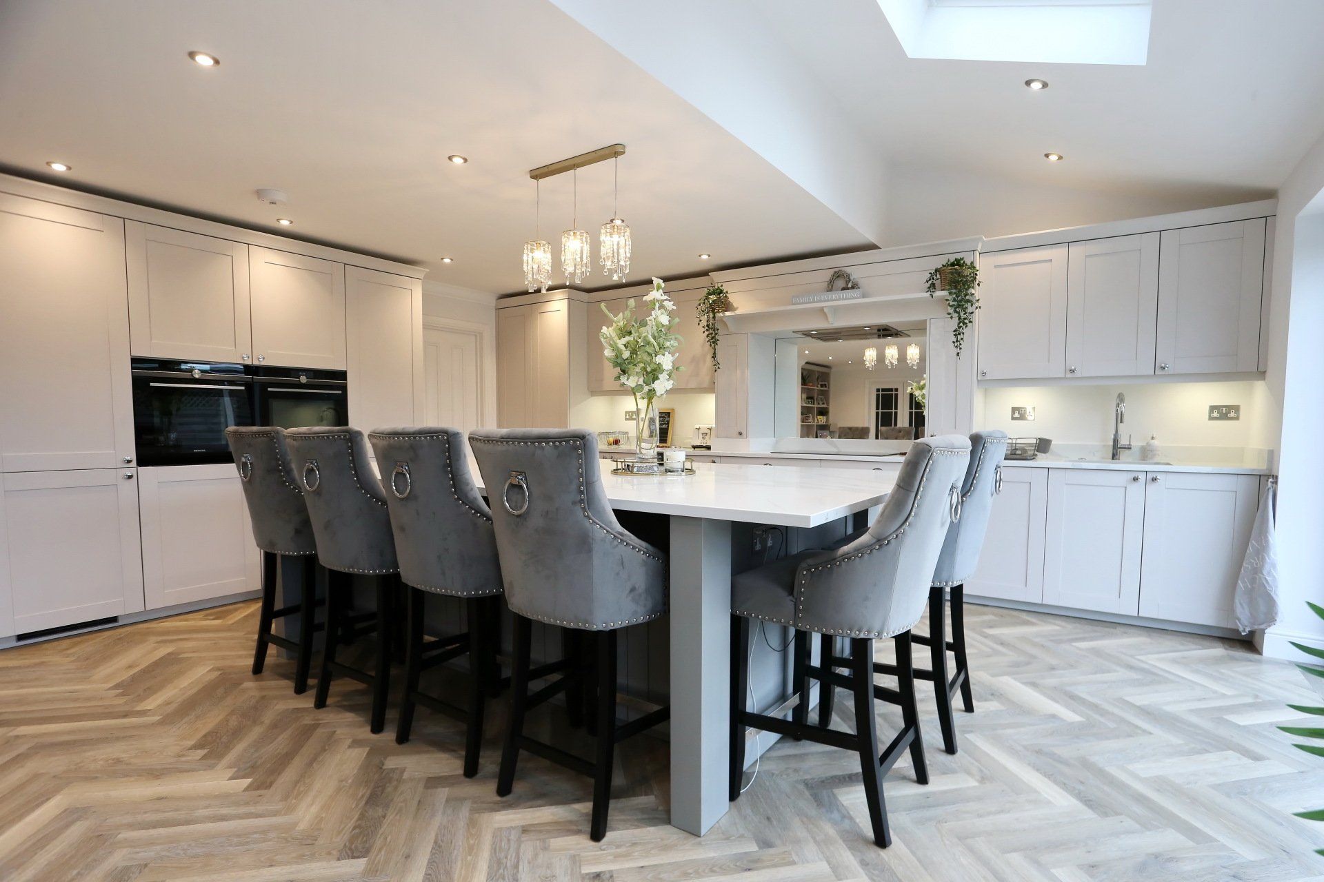 Modern kitchen with large island, light gray cabinets, and herringbone wood floor.