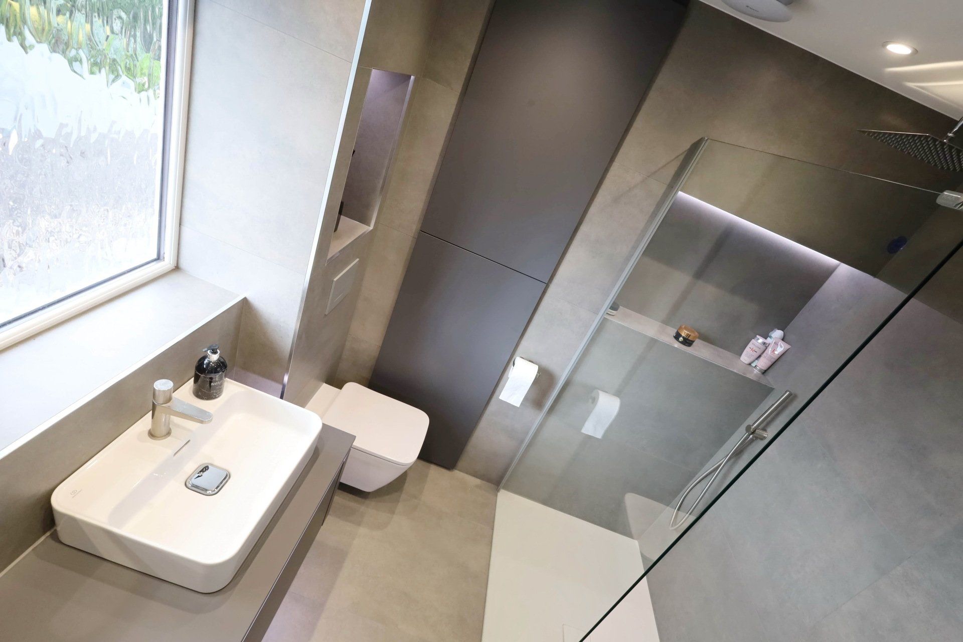 Modern bathroom with gray tiles, shower, sink, and toilet.