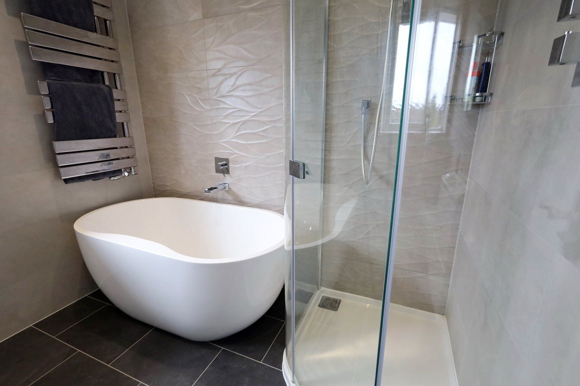Modern bathroom with a white tub, glass shower, and towel warmer.