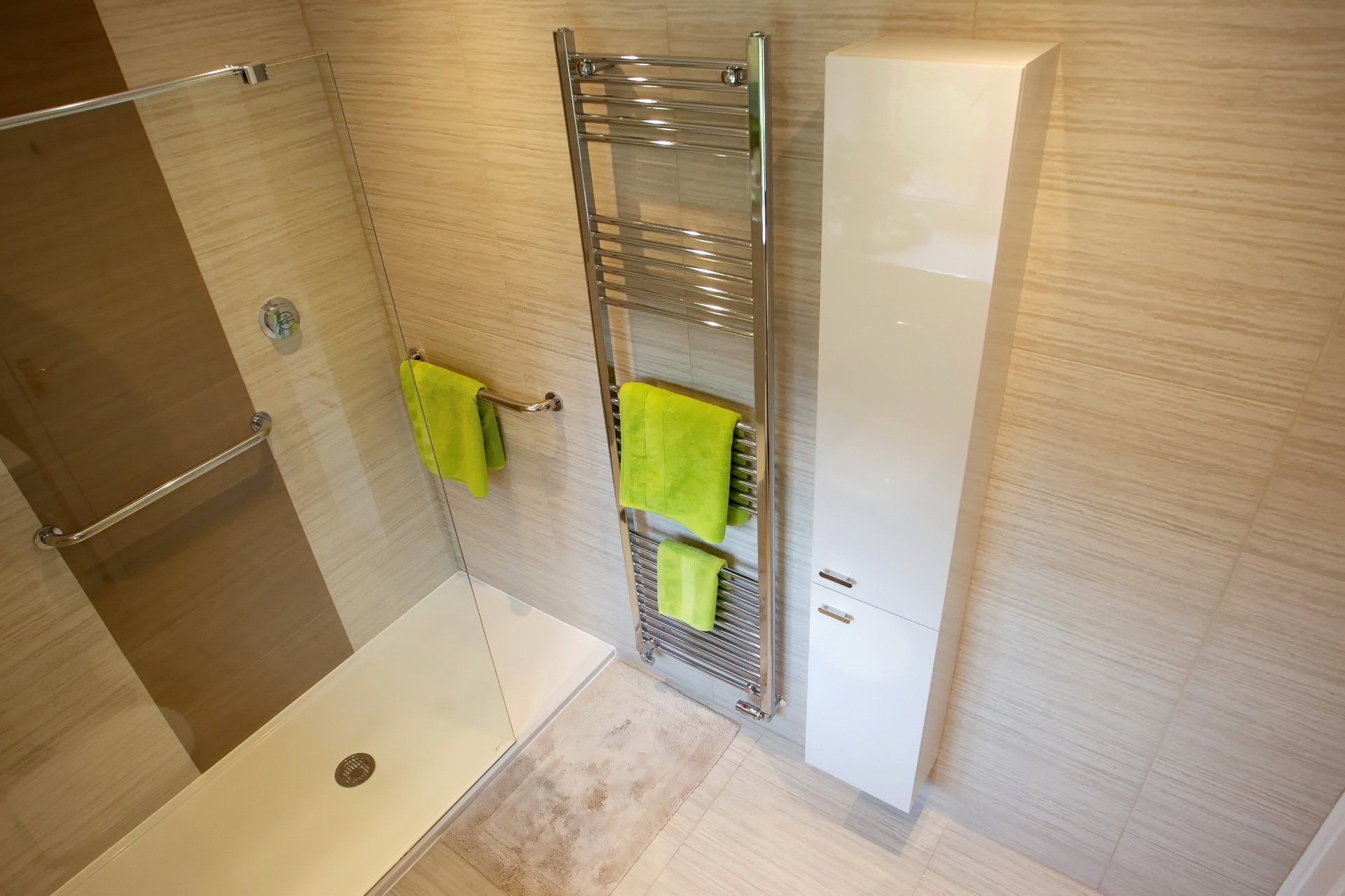 Bathroom with shower, towel rack with green towels, and tall white cabinet.