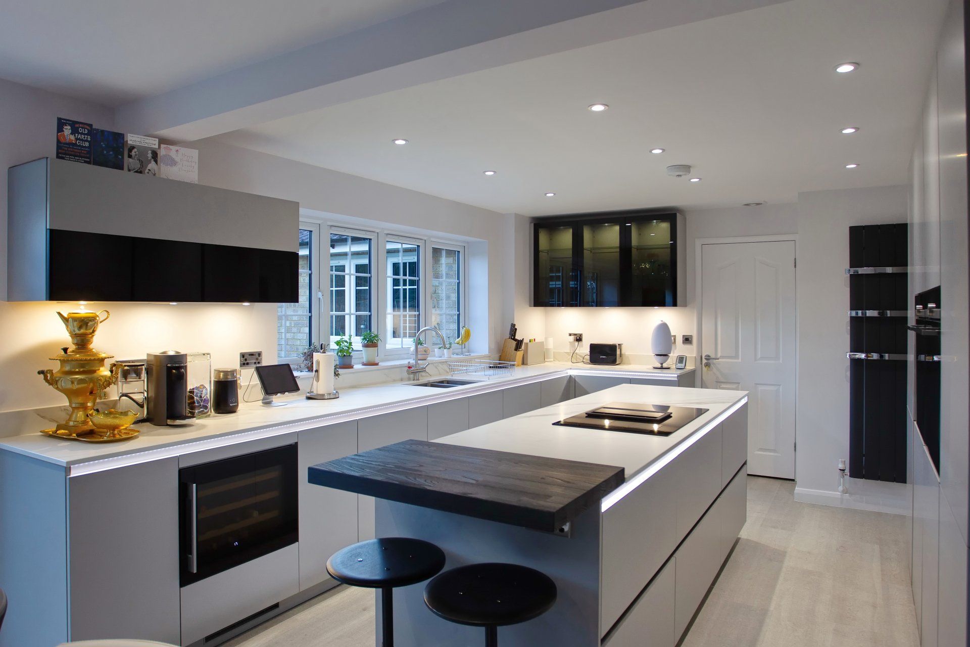 Modern gray kitchen with island, white countertops, and black accents; bright with recessed lighting.
