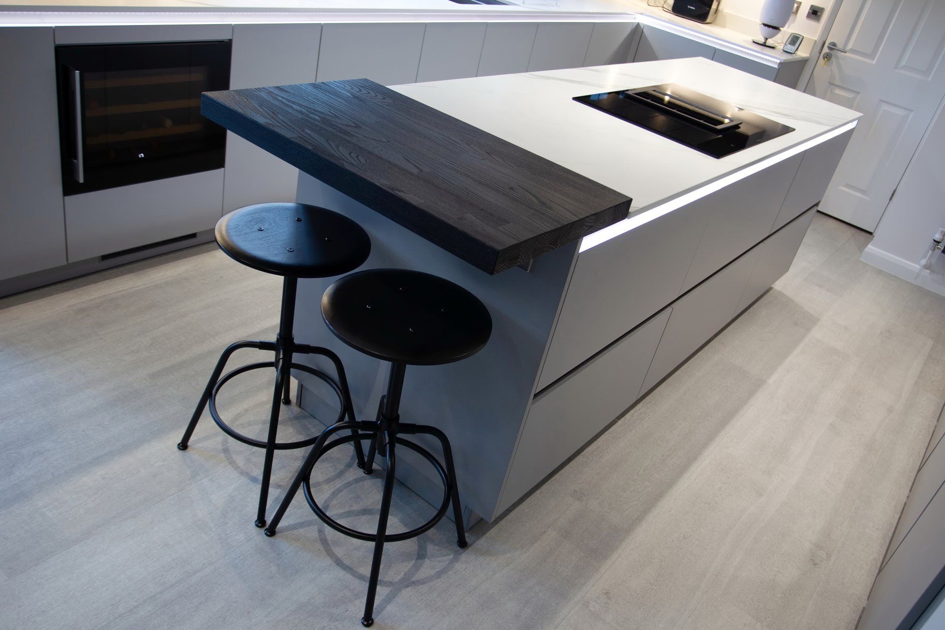 Modern kitchen island with dark wood overhang, black stools, and built-in stovetop.