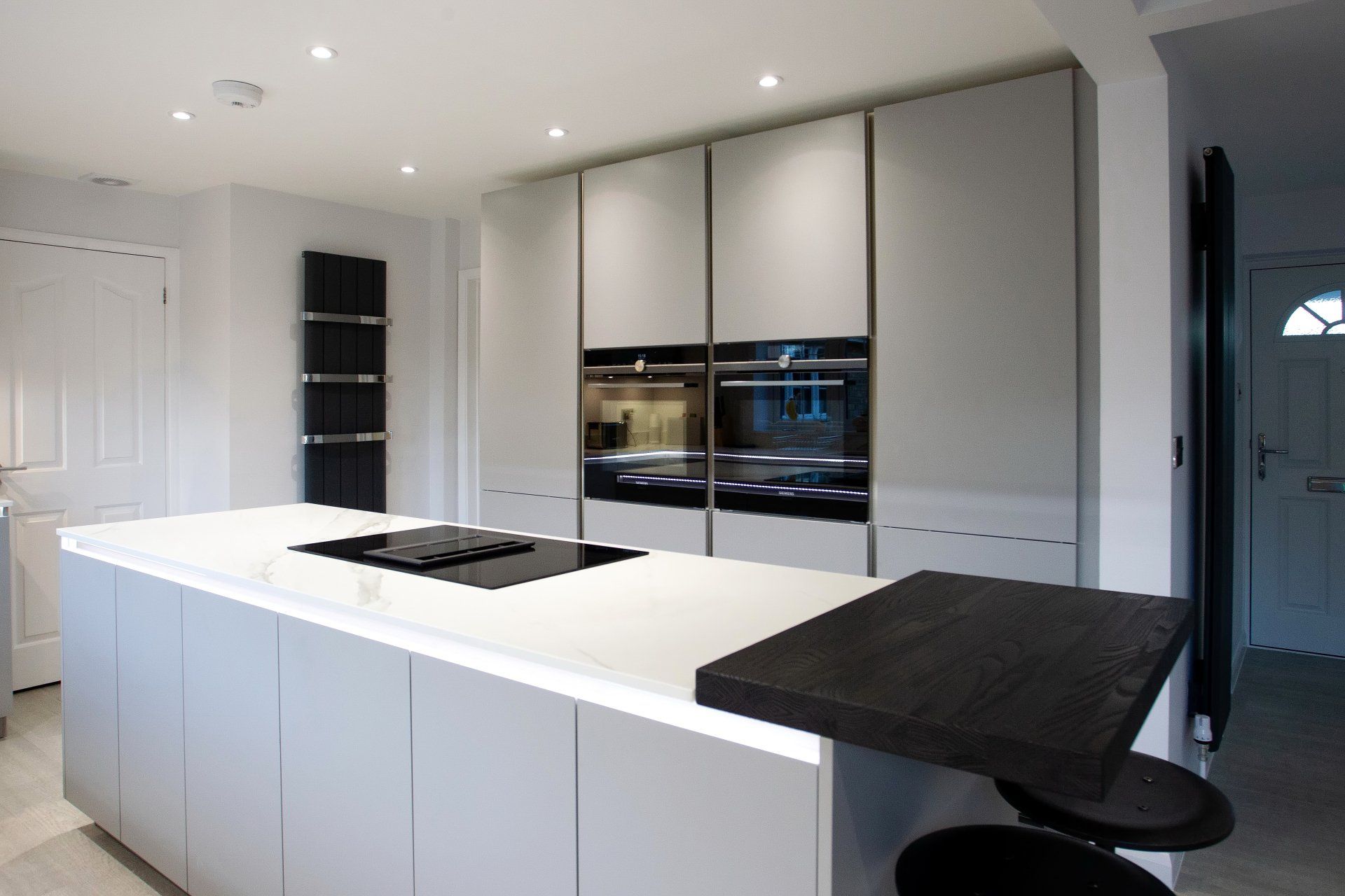Modern kitchen with gray cabinets, island with cooktop, and built-in ovens.