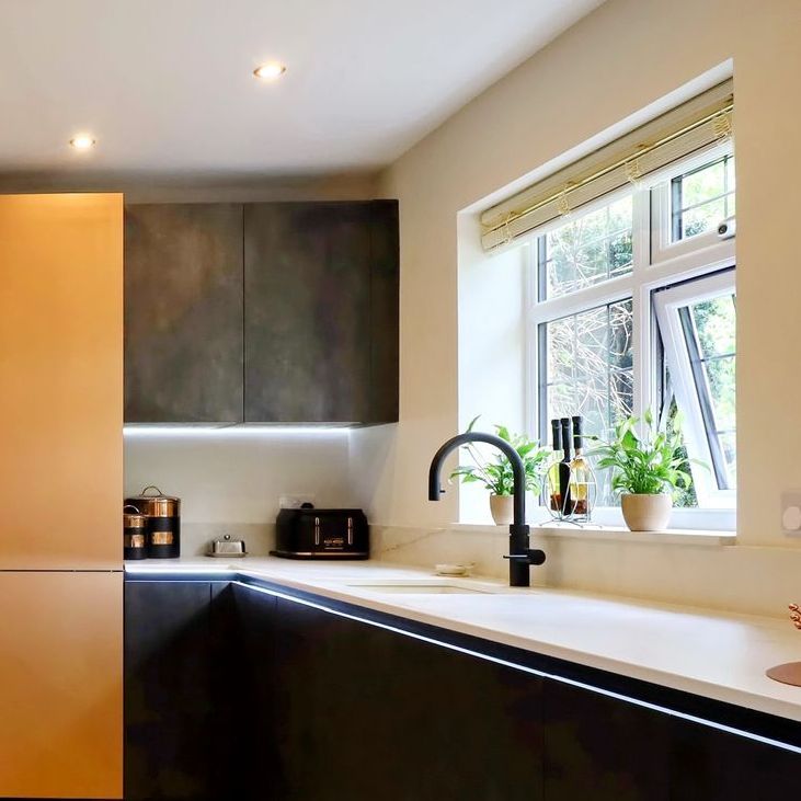 Modern kitchen with black and light cabinets, a white countertop, and a window with plants.