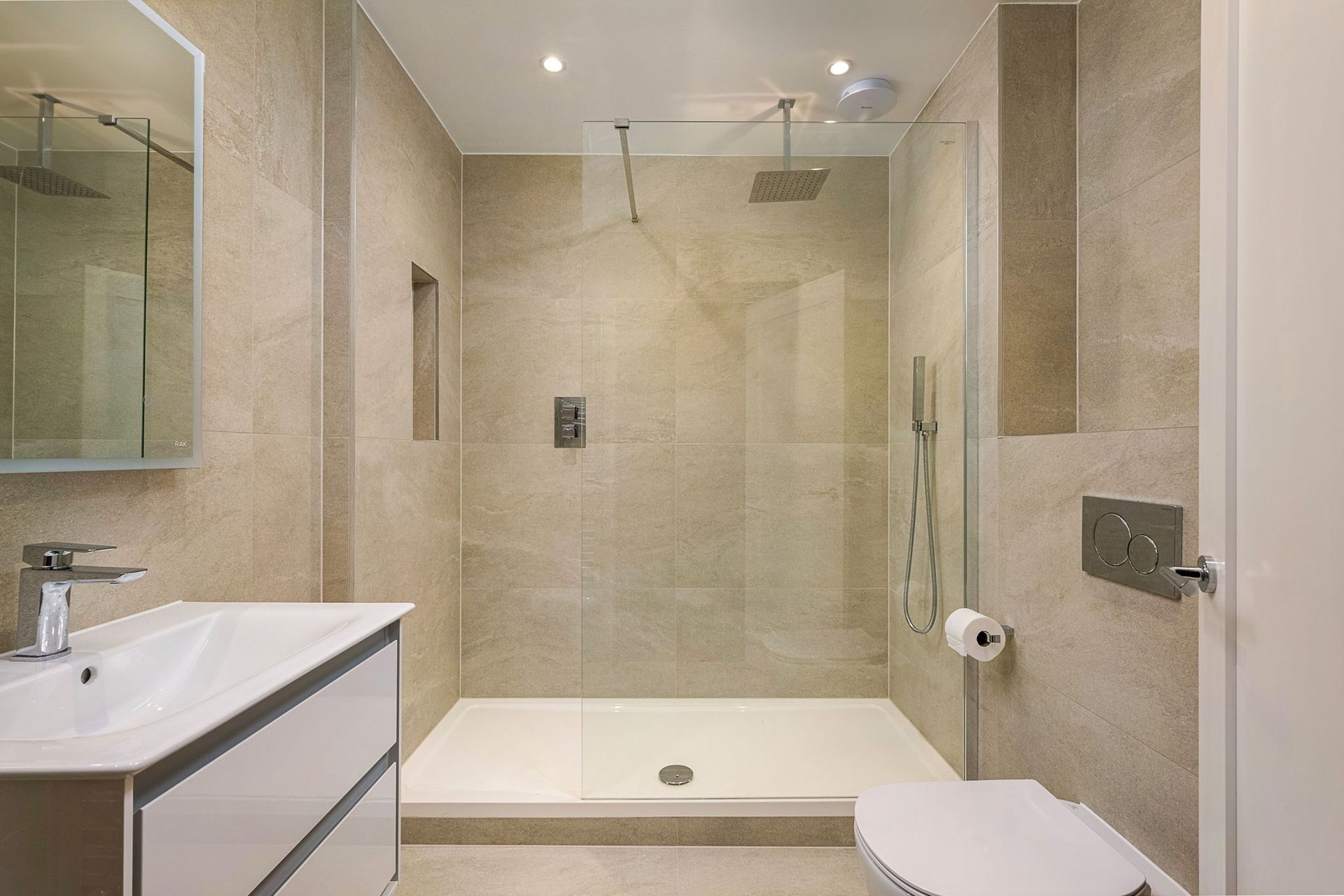 Modern bathroom with tiled walls, glass shower, white fixtures.