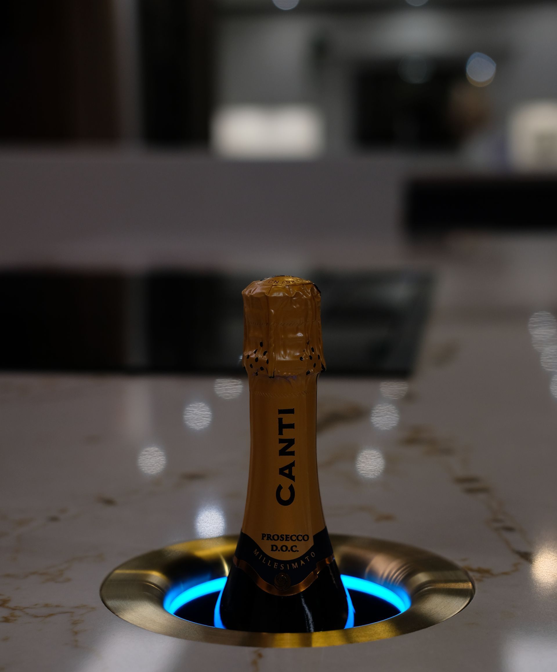 Champagne bottle in a recessed, lit holder on a counter. Bottle label reads "CANTI".