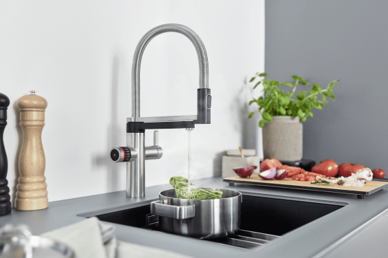 Stainless steel kitchen faucet over a sink filling a pot with water; vegetables on a cutting board nearby.