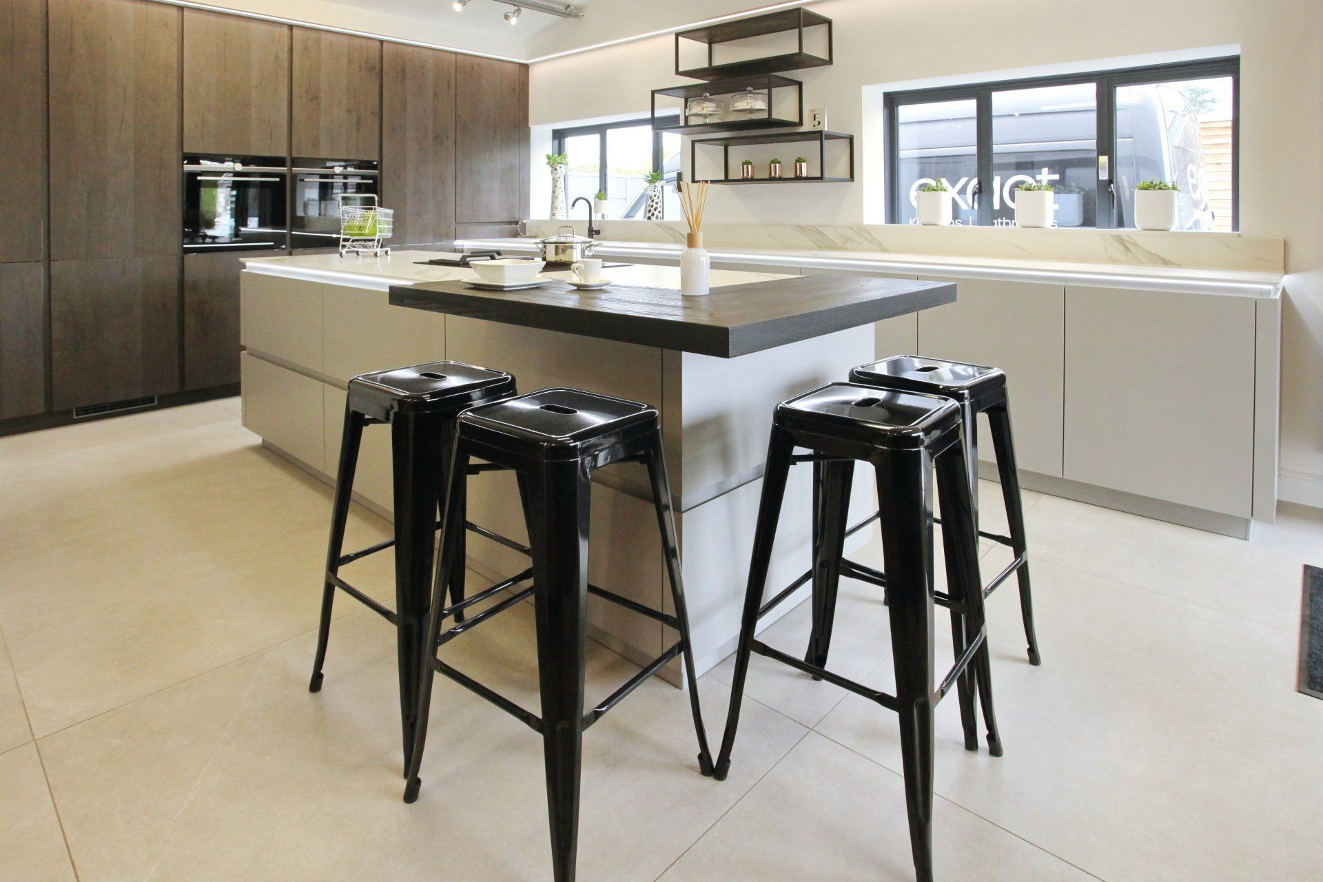 Modern kitchen with a gray island, black stools, and wood cabinetry.