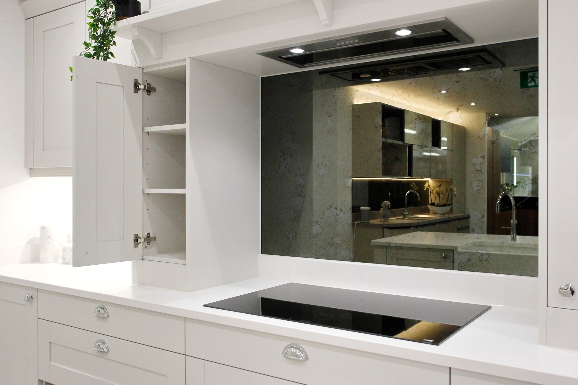 White kitchen with cooktop, mirror backsplash, and open cabinet.