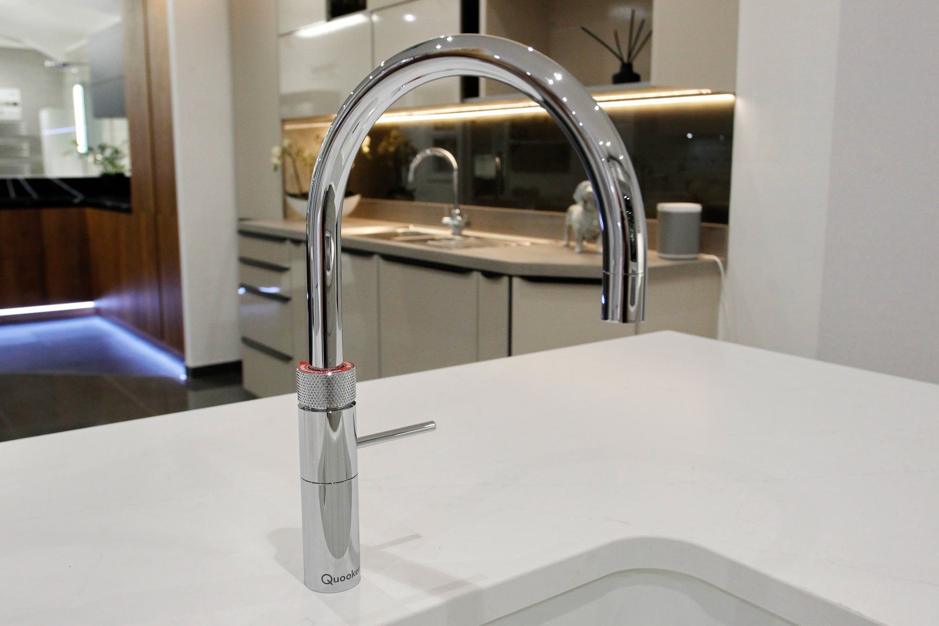 Chrome kitchen faucet with curved spout on a white countertop.