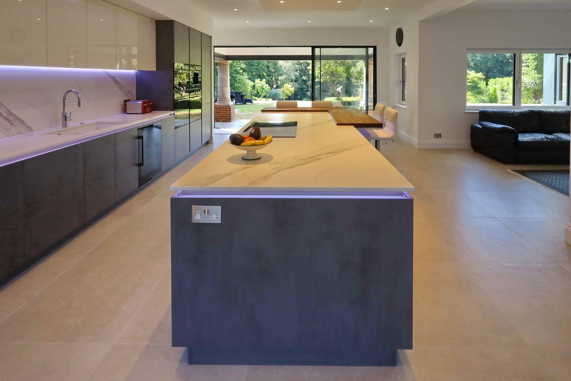 Modern kitchen with a gray island, light-colored countertops, and large windows looking outside.