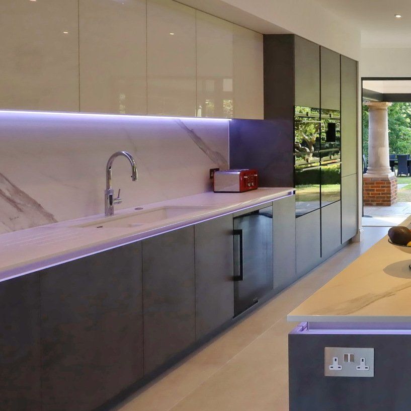 Modern kitchen with gray and white cabinets, stainless steel appliances, and under-cabinet lighting.