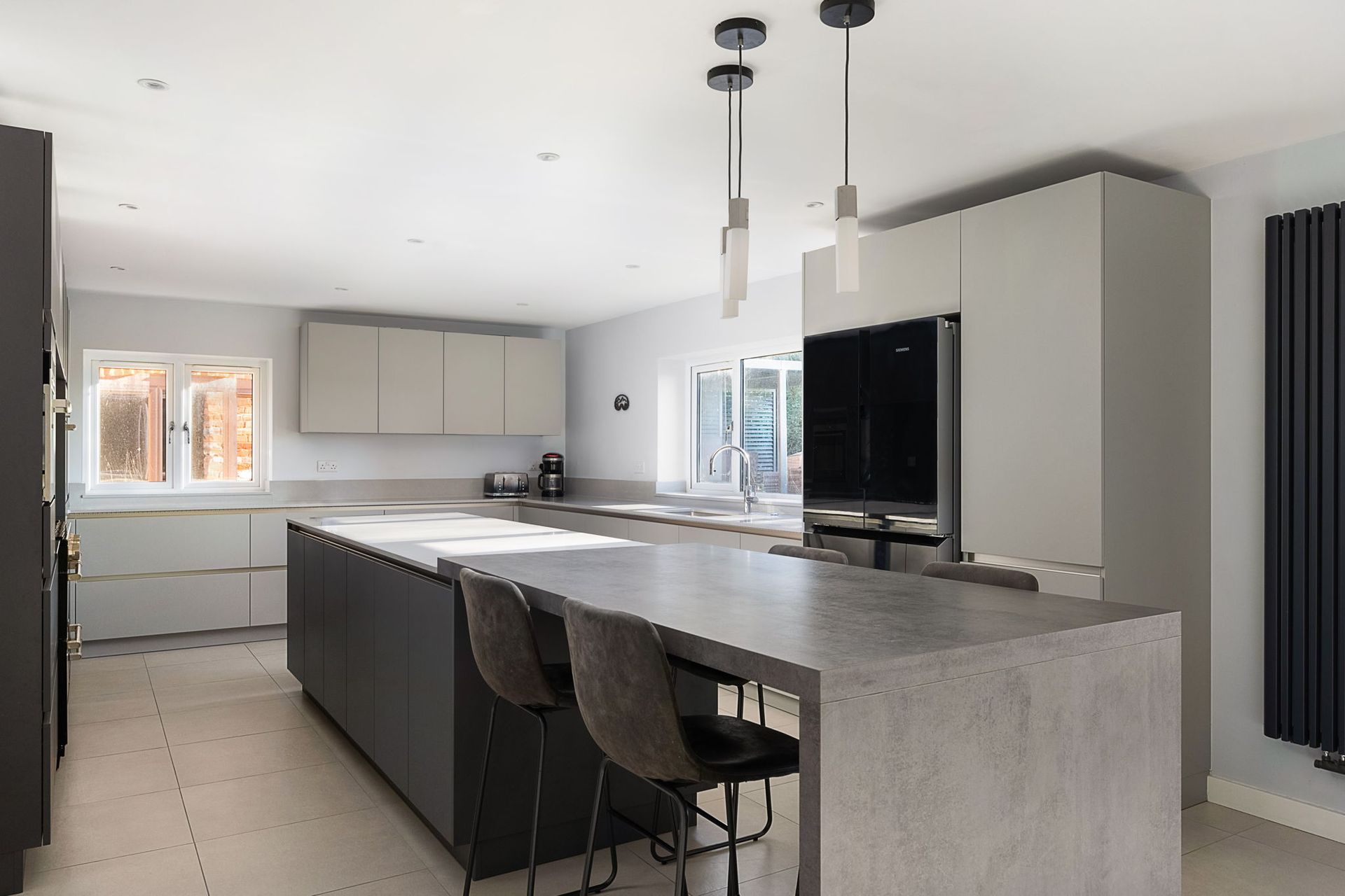 Modern kitchen with gray cabinets, large island with seating, pendant lights, and stainless steel appliances.