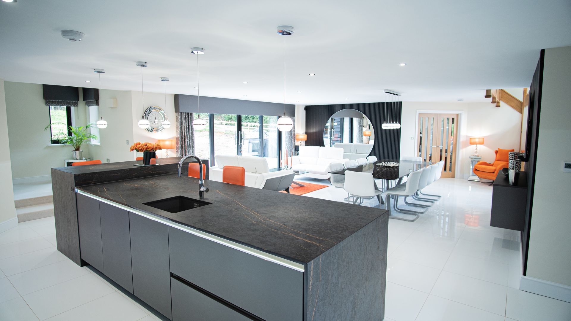 Modern open-plan kitchen and living space with black island, white flooring, and orange accents.