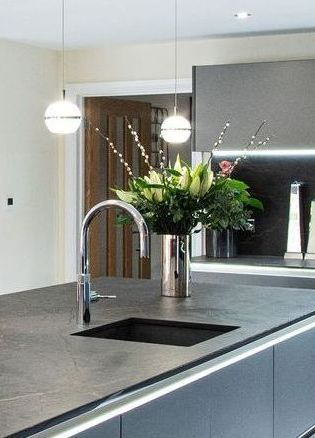 Modern kitchen island with sink, faucet, flower arrangement, and spherical pendant lights.