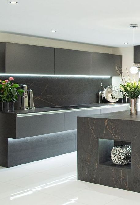 Modern kitchen with dark cabinetry, countertops, and ambient lighting; white floor.